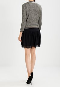 Grå stickad cardigan med rund halsringning och randig kant, tillsammans med en svart lagerkjol som har en genomskinlig, flödande nederdel.