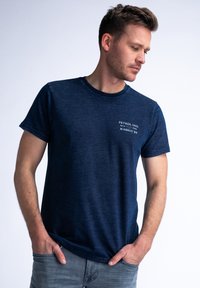 Marineblauwe T-shirt in een zachte, gestructureerde stof met een ronde hals. Heeft een klein wit logo met tekst op de linkerborst.
