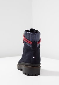 Bottine en daim bleu marine avec un col matelassé bleu marine et des lacets rouges. Dotée d'une semelle en caoutchouc noire épaisse avec motif adhérent et logo en relief.