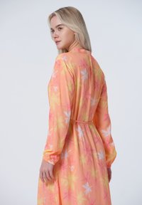 Langärmliges Kleid aus leichtem Material mit einem pastellorangefarbenen Grundton, verziert mit pinken und weißen Blumenmustern sowie einem Taillenzugdetail.