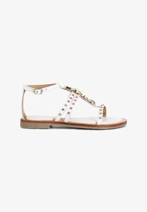 Valkoiset litteät sandaalit, joissa on ohut nauhadesign, kultaiset yksityiskohdat ja koristeelliset rose gold -niitit sivuilla. Sileä pohja, jossa on vaaleanruskeita yksityiskohtia.