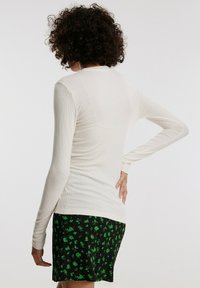 Langdurige mouw, ribgebreide crèmekleurige top gedragen met een zwarte rok met kleine groene bloemmotieven. Eenvoudig ontwerp met een aansluitende silhoeët.