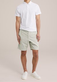 White polo shirt with a buttoned collar, paired with light green textured shorts. White sneakers complete the outfit.