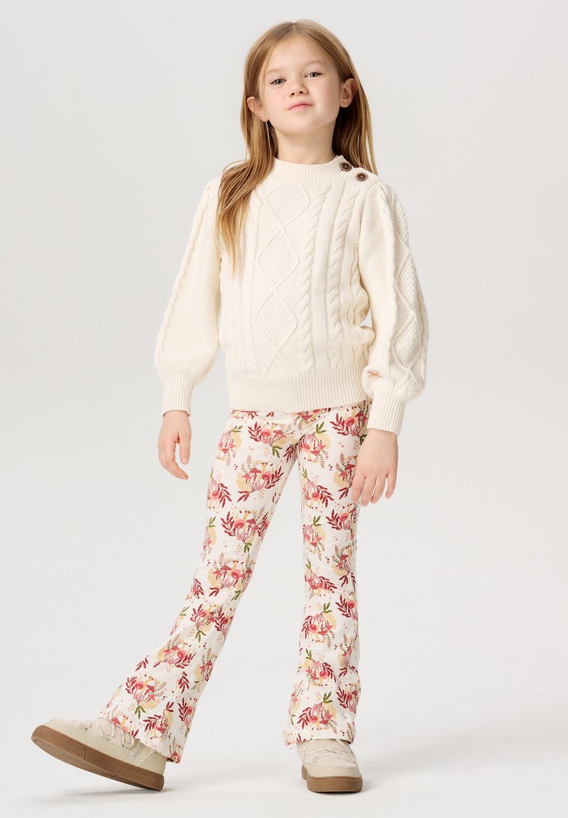 Cremefarvet striktrøje med kabelmønster og knapdetaljer, parret med blomstertrykte flared bukser i bløde pastelfarver og beige sko.