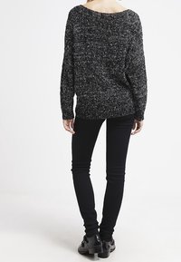 Svart och vit prickig stickad tröja, avslappnad passform, vid halsringning. Matchad med åtsittande svarta jeans och svarta läderstövletter.