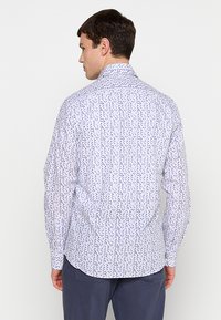 Langekorte mouwshirt van witte stof met een blauw en paars stippenpatroon. Heeft een klassieke kraag en een knoopsluiting op de rug.
