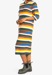 Persona vistiendo un vestido midi de punto a rayas multicolores con mangas tres cuartos y botines grises con un borde estampado.