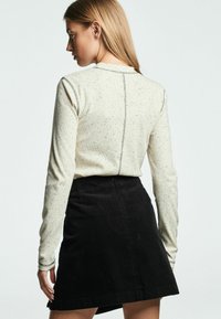 Top crem cu mâneci lungi, presărat cu pete negre, având o cusătură pe spate, asortat cu o fustă din catifea neagră, cu textură netedă și stil ajustat.