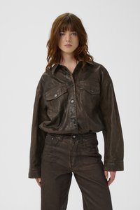 Tamsiai ruda odinė striukė su sagomis priekyje, krūtinės kišenėmis ir laisvo kirpimo. Derinama su tamsiai rudomis džinsais, kad sukurtų vientisą įvaizdį.