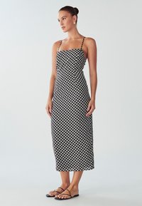 Čiernobiele vzorované midi šaty s tenkými ramienkami, priliehajúcim korzetom, rovnou siluetou a hladkou látkou; nosené s čiernymi plochými sandálmi.