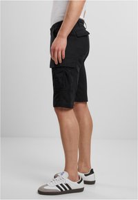Shorts cargo noirs avec plusieurs poches, une coupe décontractée et une longueur mi-cuisse, associés à des chaussures de sport blanches et grises.
