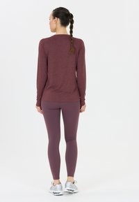 Vinröd långärmad topp med figurnära design, kombinerad med matchande vinröda leggings. Utrustad med en slät yta och silvriga sportskor.
