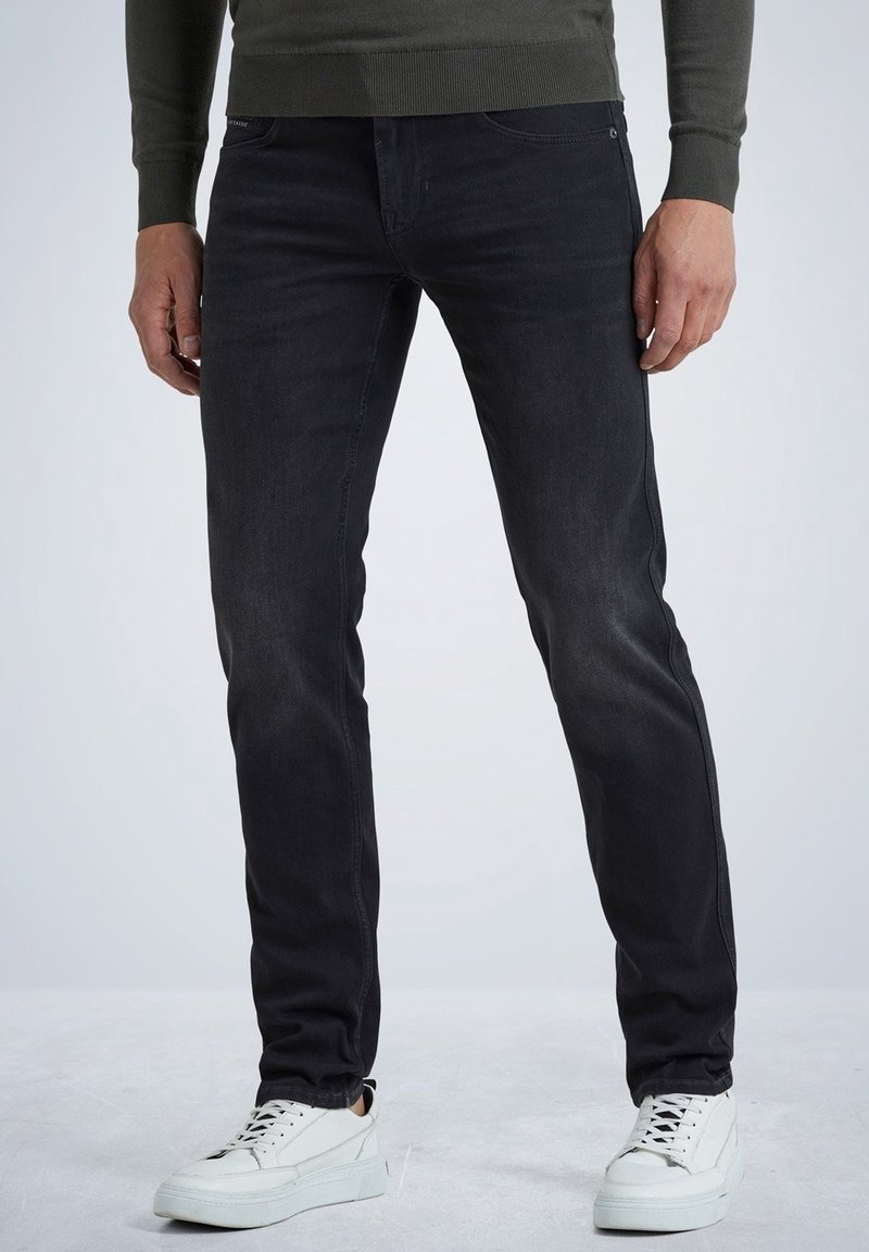 Jeans de mezclilla negra con ajuste slim, con un ligero desgaste y bolsillos frontales. Combinados con zapatillas bajas blancas.
