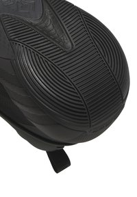 Svart gummisko sula med texturerade räfflor, featuring en framträdande central logotyp och en bakre dragflik för enkel påtagning.