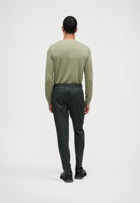 Svijetlozeleni pulover dugih rukava u kombinaciji s tamnim hlačama, ističe prilagođen dizajn. Pogled sa stražnje strane naglašava glatke teksture i suptilno krojenje.