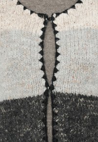 Πλεκτό πουλόβερ με λωρίδες σε ανοιχτό γκρι, σκούρο γκρι και κρέμα. Οι κυματιστές μαύρες άκρες περιβάλλουν την λαιμόκοψη και το άνοιγμα.