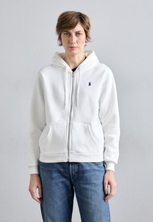 Hvitt zip-up hettegenser laget av mykt stoff med snor i hetten. Har en liten blå logo på brystet og to frontlommer.