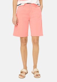 Koraalkleurige katoenen shorts met een recht model, opgerolde zoom en zijzakken. Gecombineerd met lichtbruine sandalen met een gespaccent.