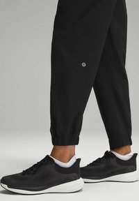 Black sneakers with a textured upper and white sole, paired with black jogger pants featuring elastic cuffs and a small logo.