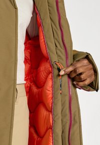 Kurtka ocieplana z brązową zewnętrzną powłoką i intensywnie pomarańczową podszewką. Wyposażona w różowy zamek błyskawiczny, pikowaną fakturę i regulowany sznurek.