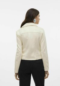Veste en cuir couleur crème avec un design ajusté, larges revers et détails de couture. Assortie à un jean noir, avec un matériel minimal visible.