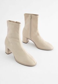 Beige ankle boots made of smooth leather, featuring a side zipper, square toe design, and a chunky block heel for stability.
