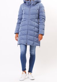 Ljusblå puffjacka med huva, quiltat mönster, dragkedja fram och sidofickor, kombinerad med blå jeans och vita sneakers.