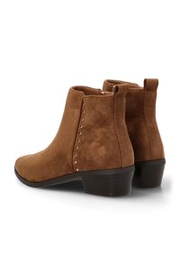 Botines de ante marrón con tacón cuadrado, que presentan detalles decorativos de studs metálicos a lo largo del costado y una puntera redondeada.