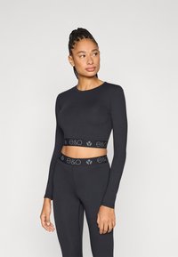 Μαύρο μακρυμάνικο crop top με στρογγυλή λαιμόκοψη και ελαστική ταινία διακοσμημένη με λογότυπο. Συνδυάζεται με αντίστοιχο κολάν ψηλόμεσο. Ελαστικό ύφασμα.