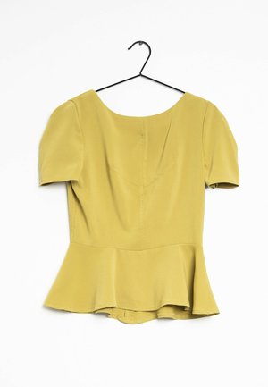 Yellow short-sleeve blouse with peplum hem hanging on a black wire hanger against a white background.