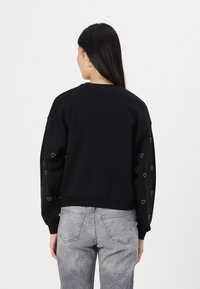 Czarny sweatshirt z długimi rękawami, z małymi sercami na rękawach. Miękki materiał, luźny krój i prążkowany ścięgno.