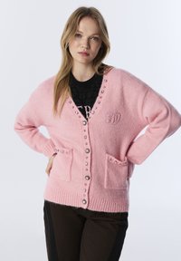 Różowy kardigan z miękkiego materiału, z dekoltem w serek, z zapięciem na guziki, ozdobami z cyrkonii i dwoma przednimi kieszeniami. Szczegółowy haft logo.