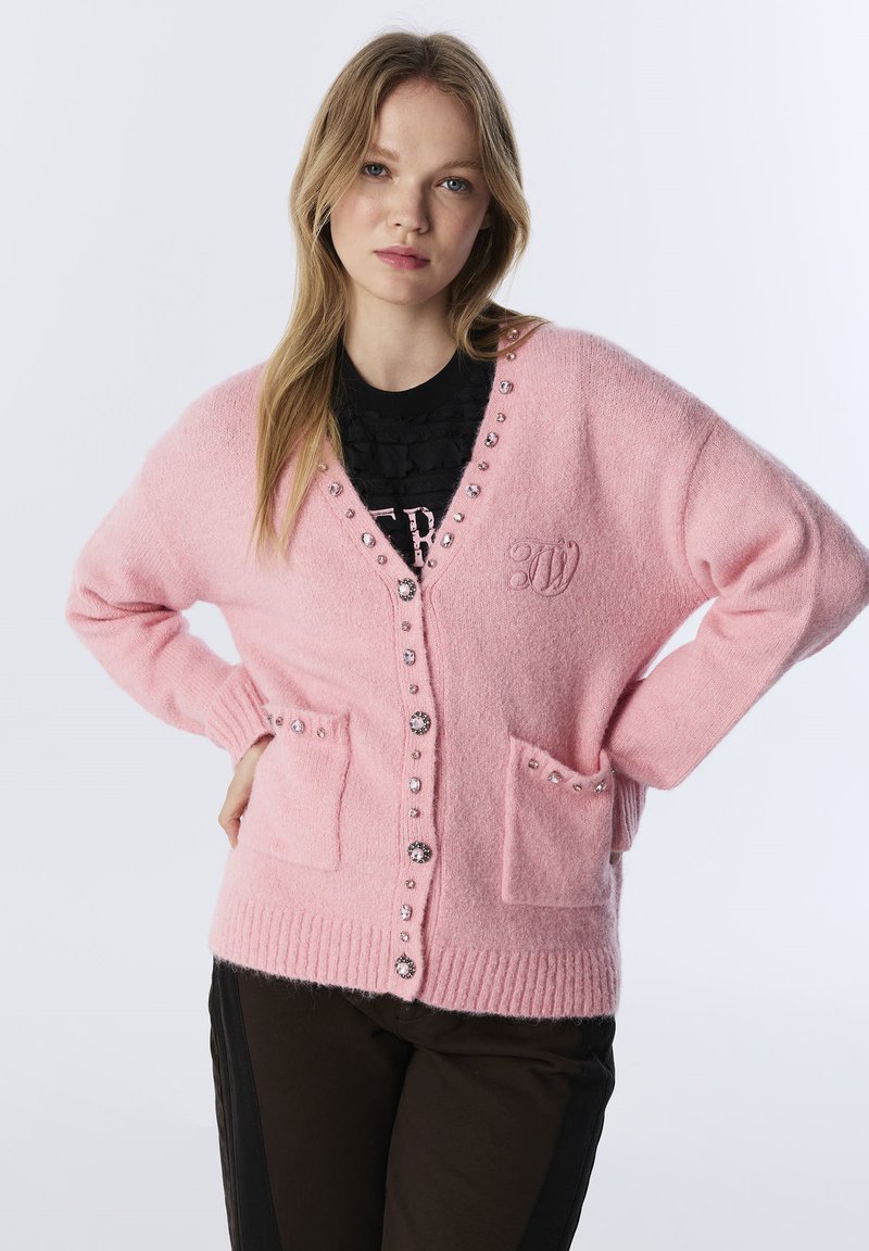Różowy kardigan z miękkiego materiału, z dekoltem w serek, z zapięciem na guziki, ozdobami z cyrkonii i dwoma przednimi kieszeniami. Szczegółowy haft logo.