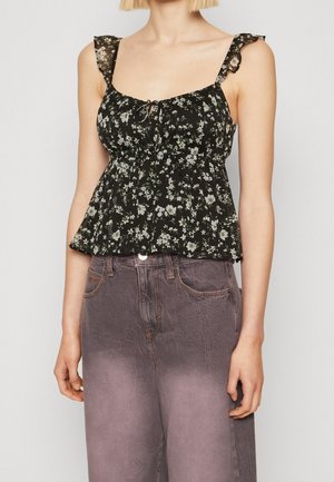 Kvinde iført en sort blomsterprintet ærmeløs top med flæse stropper og lilla falmede jeans med højtaljet pasform.