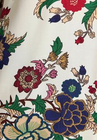 Floral fabric with a white background featuring red, blue, and green flowers, detailed leaves, and contrasting outlines in earthy tones.