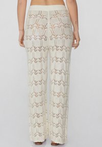 Crème-kleurige gehaakte gebreide broek met een wijde pijpdesign, voorzien van een textuurpatroon en een elastische tailleband.