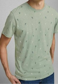 Groen T-shirt met korte mouwen gemaakt van zachte stof, met een patroon van kleine kamerplanten in blauw en wit. Ronde halslijn en standaard pasvorm.