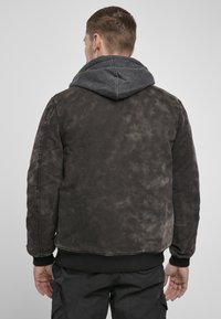 Černá bombardérka s opotřebovanou texturou, disponující šedou kapucí, pružnými manžetami a páskem. Jednoduchý, praktický design.