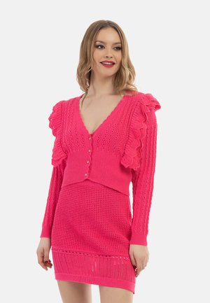 Cardigan roz tricotat cu accente franjurate, închidere cu buton și decolteu în formă de V, asortat cu o fustă texturată. Ambele sunt fabricate dintr-un material moale.