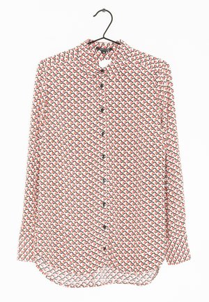 Langærmet skjorte med knapper og et gentaget geometrisk mønster i rødt, sort og hvidt, hængende på en sort bøjle.