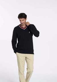 Pull en tricot noir avec un col en V et des détails en rayures rouges et blanches. Dispose d'un motif texturé et d'un petit logo sur la poitrine.