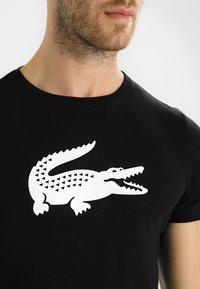 T-shirt nera con una grande grafica di un coccodrillo bianco caratterizzato da motivi triangolari e con la bocca aperta, collo rotondo e maniche corte.