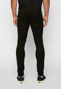 Melni pieguļoši džinsi, izgatavoti no džinsa, ar piecu kabatu dizainu, gludu virsmu un minimālām izšūšanas detaļām aizmugurē.