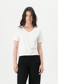 White cotton t-shirt with a v-neck, short sleeves, and a cropped fit, paired with black high-waisted pants. Simple and minimalist design.