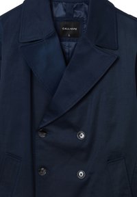 Cappotto blu navy doppiopetto con ampi revers, quattro bottoni neri, tasche laterali e etichetta del brand "Calliope" all'interno del colletto.