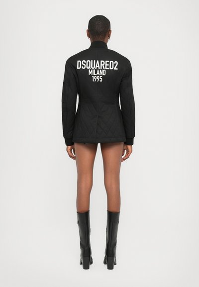 Veste matelassée noire avec col montant et manches longues, affichant le texte blanc "DSQUARED2 MILANO 1995" au dos.