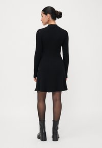 Robe noire à côtes avec des manches longues, corsage ajusté et jupe évasée. Associée à des bottes en cuir noires à talons jusqu'aux genoux.