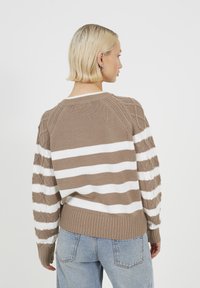 Brązowy i biały sweter w paski z teksturowanym splotem, z raglanowymi rękawami i ściągaczem, w połączeniu z niebieskimi dżinsami.