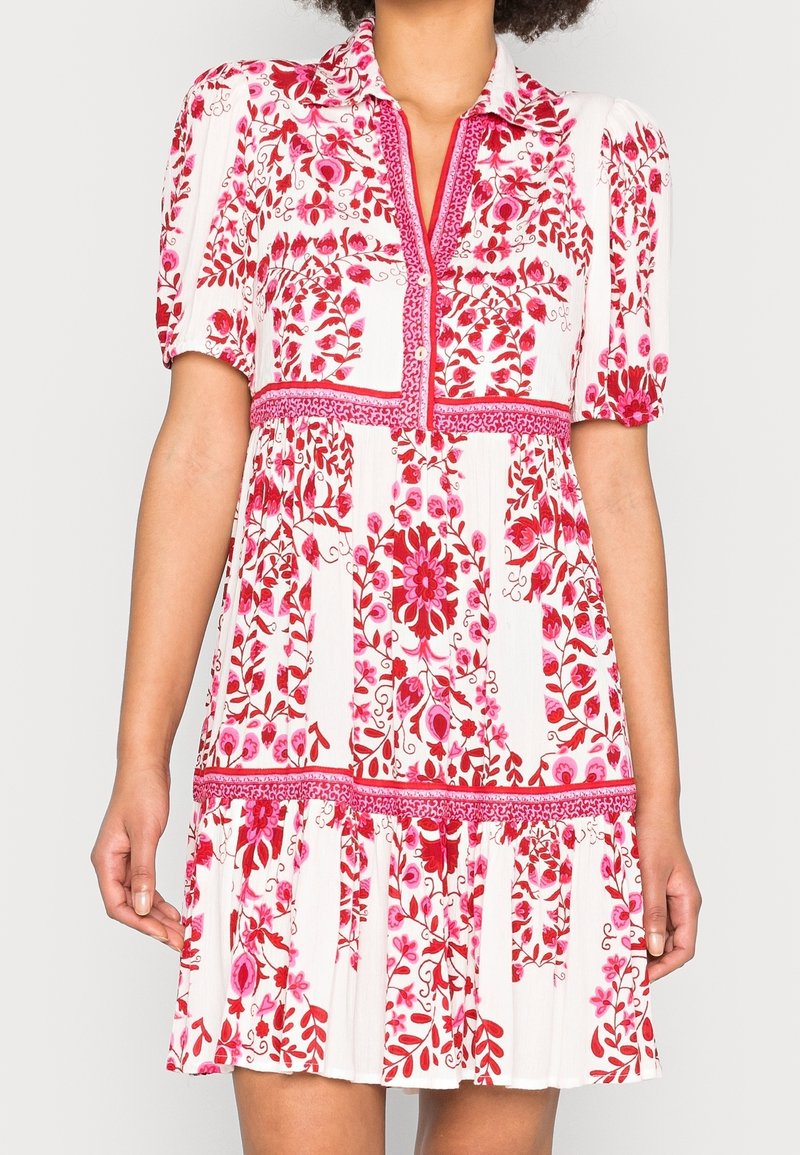 Robe blanche à manches courtes avec motifs floraux rouges et roses, dotée d'un col, d'une patte de boutonnage et de détails froncés à la taille et à l'ourlet.