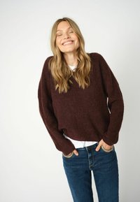 Bordeauxrood gebreid sweater met een losse pasvorm en verlaagde schouders, gecombineerd met een wit shirt en blauwe jeans. Soepele textuur, casual design.